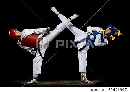 Dynamic portrait of two young women, taekwondo athletes training together isolated over dark background. Concept of sport, skills 85691997