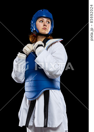 Portrait of young girl, taekwondo practitioner posing isolated over dark background. Concept of sport, skills 85692024