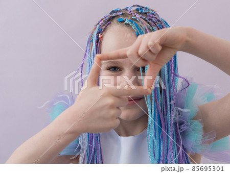A teenage girl looks into the camera through a frame of fingers. A fashionable gesture. Photos for social networks A teenage girl looks into the camera through a frame of fingers. A fashionable gesture. Photos for social networks 85695301