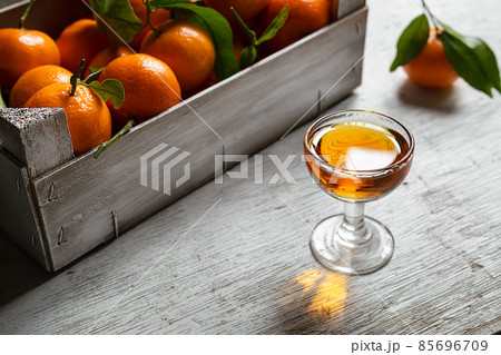 Tangerine liqueur shot and a box with fresh tangerines on on a white wooden table 85696709