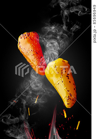 Two grilled peppers hovering over flames in sparks and haze on black background Two grilled peppers hovering over flames in sparks and haze on black background 85696949