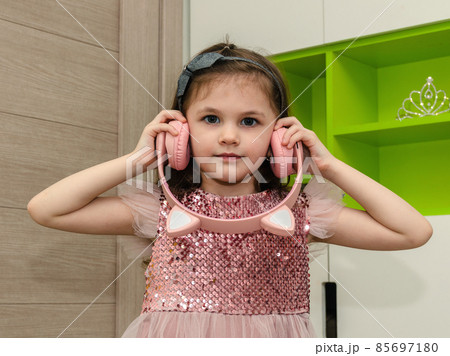 Little girl in a pink dress listening to wireless headphones at home. 85697180