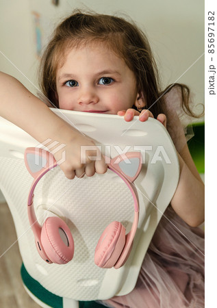 Little girl in a pink dress listening to wireless headphones at home. 85697182