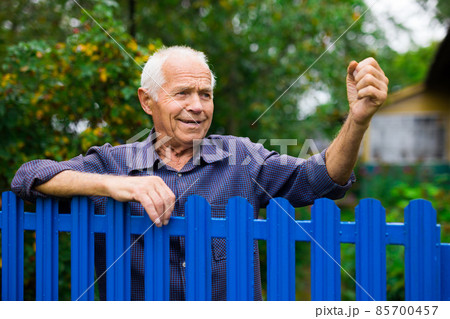 Old man showing fist outdoors beside fence 85700457