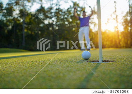 Golfer action to win after long putting golf ball on the green golf, lens flare on sun set evening time. 85701098