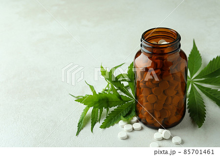 Bottle with pills and cannabis leaves on white textured background 85701461