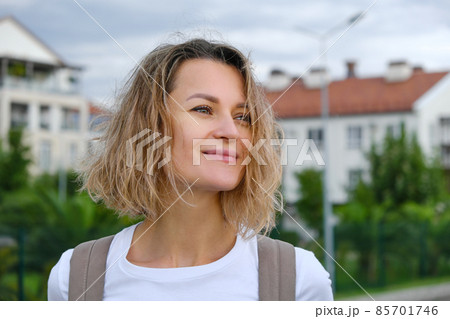 Pretty smiling curly caucasian woman in casual look confidently walks down the street with backpack. White t-short and blue denim skirt. Joy of life, active lifestyle, fashion blogger. 85701746