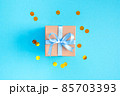 Gift box with a blue bow on a blue background with gold confetti. Flat lay composition for birthday or holiday. 85703393