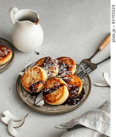 Syrniki or cottage cheese fritters with with chocolate sauce and coconut on ceramics plate 85705029