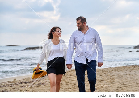 Happy middle-aged couple walking together on the beach. Happy middle-aged couple walking together on the beach. 85706889