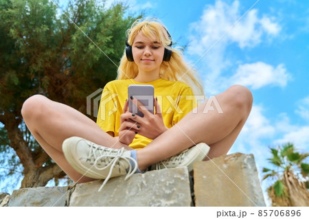 Teenage girl in headphones looking in smartphone 85706896