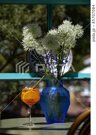 Summer refreshment aperitif cocktail in wine glass with ice rocks, bamboo straw and sliced oranges on a table in tropical summer garden 85707084