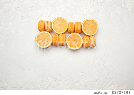 Orange French Macaroons with orange fruit filling on a creamy white clay background, decorated with fresh sliced oranges 85707193