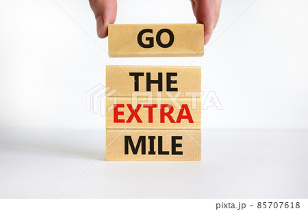 Go the extra mile symbol. Concept words Go the extra mile on wooden blocks. Businessman hand. Beautiful white table, white background, copy space. Business and go the extra mile concept. Go the extra mile symbol. Concept words Go the extra mile on wooden blocks. Businessman hand. Beautiful white table, white background, copy space. Business and go the extra mile concept. 85707618