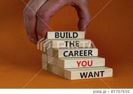 Build good career symbol. Wooden blocks with words 'build the career you want'. Businessman hand. Beautiful orange background, copy space. Business, build the career you want concept. 85707650
