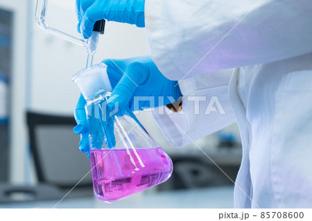Close up scientist uses a titration method of analysis to study the chemical properties of the water sample. Scientist holding Erlenmeyer flask with pink solution Close up scientist uses a titration method of analysis to study the chemical properties of the water sample. Scientist holding Erlenmeyer flask with pink solution 85708600