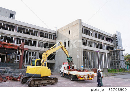 解体している老朽化した公共建造物から出たガレキをクレーン付きトラックに積む重機 解体している老朽化した公共建造物から出たガレキをクレーン付きトラックに積む重機 85708900