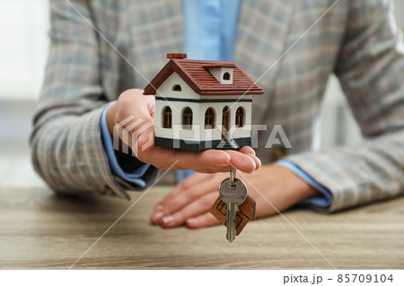 Real estate agent holding house model and key at wooden table, closeup 85709104