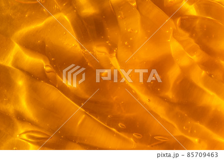 Texture of transparent yellow gel with air bubbles and waves on orange background. Concept of skin moisturizing, body care and prevention of covid19. Liquid beauty product closeup. Backdrop, flat lay Texture of transparent yellow gel with air bubbles and waves on orange background. Concept of skin moisturizing, body care and prevention of covid19. Liquid beauty product closeup. Backdrop, flat lay 85709463