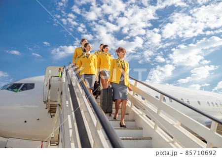 Cheerful stewardesses walking down airplane stairs under cloudy sky Cheerful stewardesses walking down airplane stairs under cloudy sky 85710692