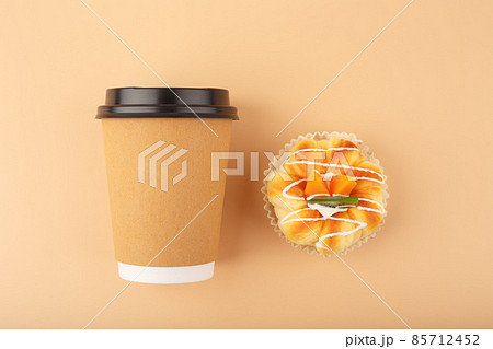 Top view of coffee or tea in brown cardboard cup with pastry against beige background 85712452