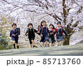 桜の咲く公園を走る新一年生 85713760