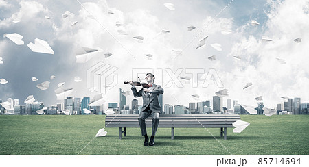 Handsome violinist in park on wooden bench play his melody 85714694