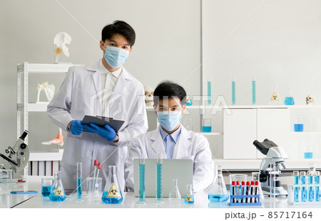Two scientists with face mask and gown working in laboratory. Omicron strain testing process, Coronavirus disease 2019. Two scientists with face mask and gown working in laboratory. Omicron strain testing process, Coronavirus disease 2019. 85717164