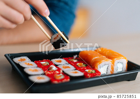 Close-up front view hands of unrecognizable young man holding sushi with chopsticks sitting at desk. Close-up front view hands of unrecognizable young man holding sushi with chopsticks sitting at desk. 85725851