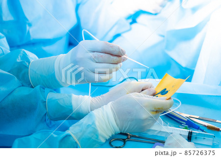 The surgeon's hand in a sterile glove holds a fibrin glue dispenser. 85726375