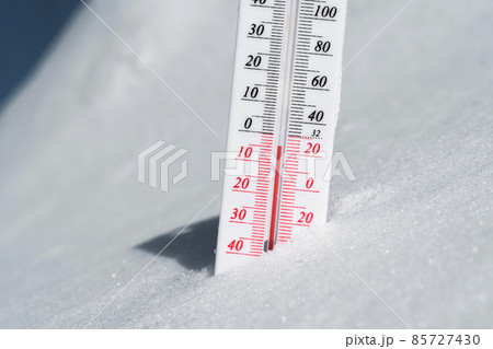 The thermometer lies on the snow and shows a negative temperature in cold weather on the blue sky.Meteorological conditions with low air and ambient temperatures.Climate change and global warming 85727430