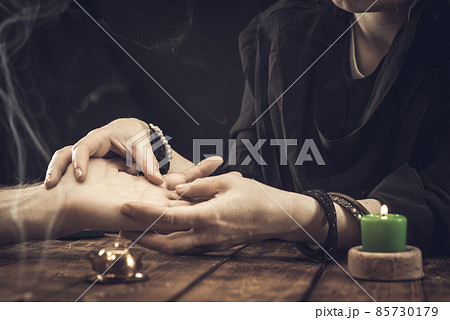 A fortune teller or oracle in search of the lines of fate in the palm of a person. Fortune telling by hand, predicting the future A fortune teller or oracle in search of the lines of fate in the palm of a person. Fortune telling by hand, predicting the future 85730179