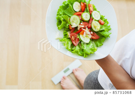 Woman measures weight on electronic scales and diet salad 85731068