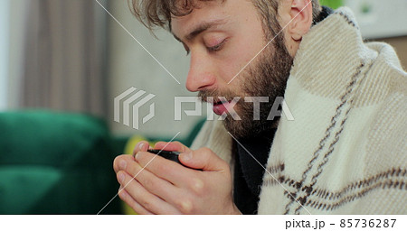 Sick young man covered with warm blanket got flu virus caught cold drinking hot tea at home. Respiratory infections disease concept. 85736287