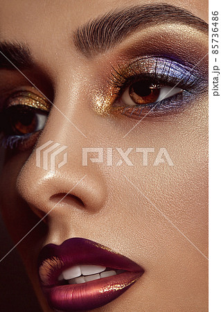 Brunette lady with luxury makeup and perfect skin is looking away. Blue and golden eyeshadow, long eyelashes, glossy lips and white teeth. Close up 85736486