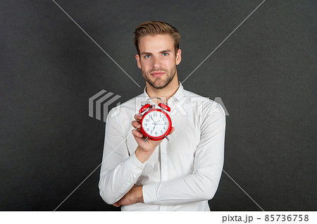 Serious guy holding alarm clock dark background, time 85736758