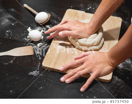 Woman kneads dough with flour and eggs on black wooden table. Cooking at home. Woman kneads dough with flour and eggs on black wooden table. Cooking at home. 85737450