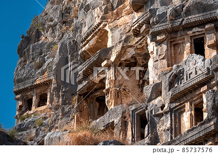 fragment of famous complex of rock tombs in the ruins of Myra of Lycia with reliefs on the cliff fragment of famous complex of rock tombs in the ruins of Myra of Lycia with reliefs on the cliff 85737576