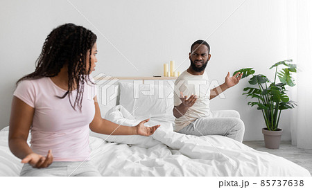 Sad angry young african american woman swears with her husband in comfortable bed in bedroom interior, panorama Sad angry young african american woman swears with her husband in comfortable bed in bedroom interior, panorama 85737638