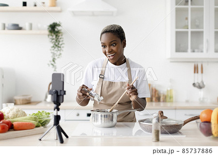 Cheerful young african american woman in apron preparing eat and recording video for food channel Cheerful young african american woman in apron preparing eat and recording video for food channel 85737886