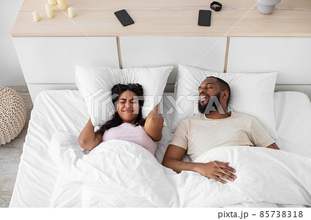 Angry upset young african american wife covers ears with pillow and suffers from husband noise Angry upset young african american wife covers ears with pillow and suffers from husband noise 85738318