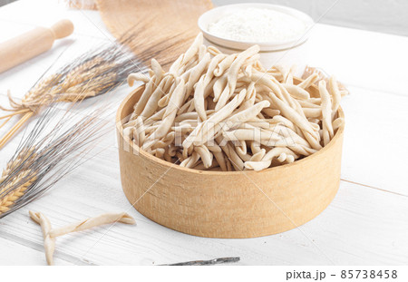 Whole grain wheat raw apulian pasta called Pizzarieddi or maccaruni in a sieve on white wooden table Whole grain wheat raw apulian pasta called Pizzarieddi or maccaruni in a sieve on white wooden table 85738458