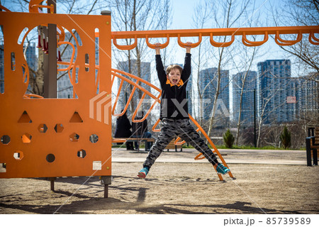 Cute boy is climbing on the playground in the schoolyard. He has a very happy face and enjoy this adventure sports alone outdoor. Warm sunny day Cute boy is climbing on the playground in the schoolyard. He has a very happy face and enjoy this adventure sports alone outdoor. Warm sunny day 85739589