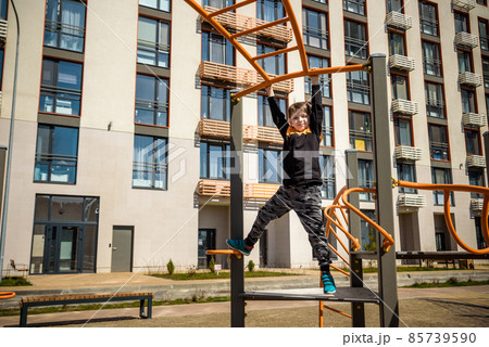 Cute boy is climbing on the playground in the schoolyard. He has a very happy face and enjoy this adventure sports alone outdoor. Warm sunny day 85739590