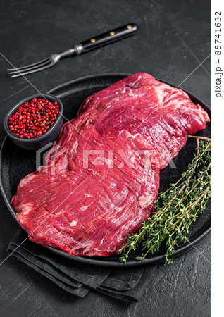 Flank or flap raw beef steak on plate with thyme. Black background. Top view 85741632