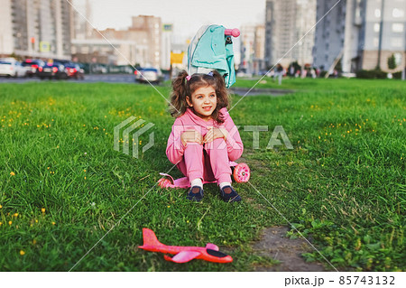 happy little girl in pink sportswear girl sitting on scooter on grass in city 85743132