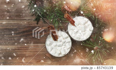 Two christmas white drink eggnog with marshmallow and cinnamon sticks on woodn brown background with spruce branches, snow, bokeh, 16:9 Two christmas white drink eggnog with marshmallow and cinnamon sticks on woodn brown background with spruce branches, snow, bokeh, 16:9 85743139