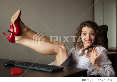 Portriat of brunette with legs on office table with laptop, hot woman in red shoes on high heels sitting at the desk. Concept of seductive secretary, female fashion, relax at work Portriat of brunette with legs on office table with laptop, hot woman in red shoes on high heels sitting at the desk. Concept of seductive secretary, female fashion, relax at work 85743431