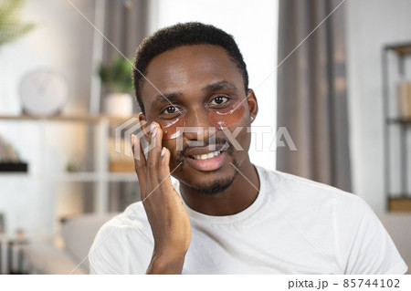 A happy and beautiful African man uses patches to rejuvenate the skin under eyes A happy and beautiful African man uses patches to rejuvenate the skin under eyes 85744102