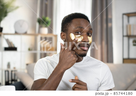 A close-up portrait of a smiling likable African American man in a white T-shirt with eye patches A close-up portrait of a smiling likable African American man in a white T-shirt with eye patches 85744180
